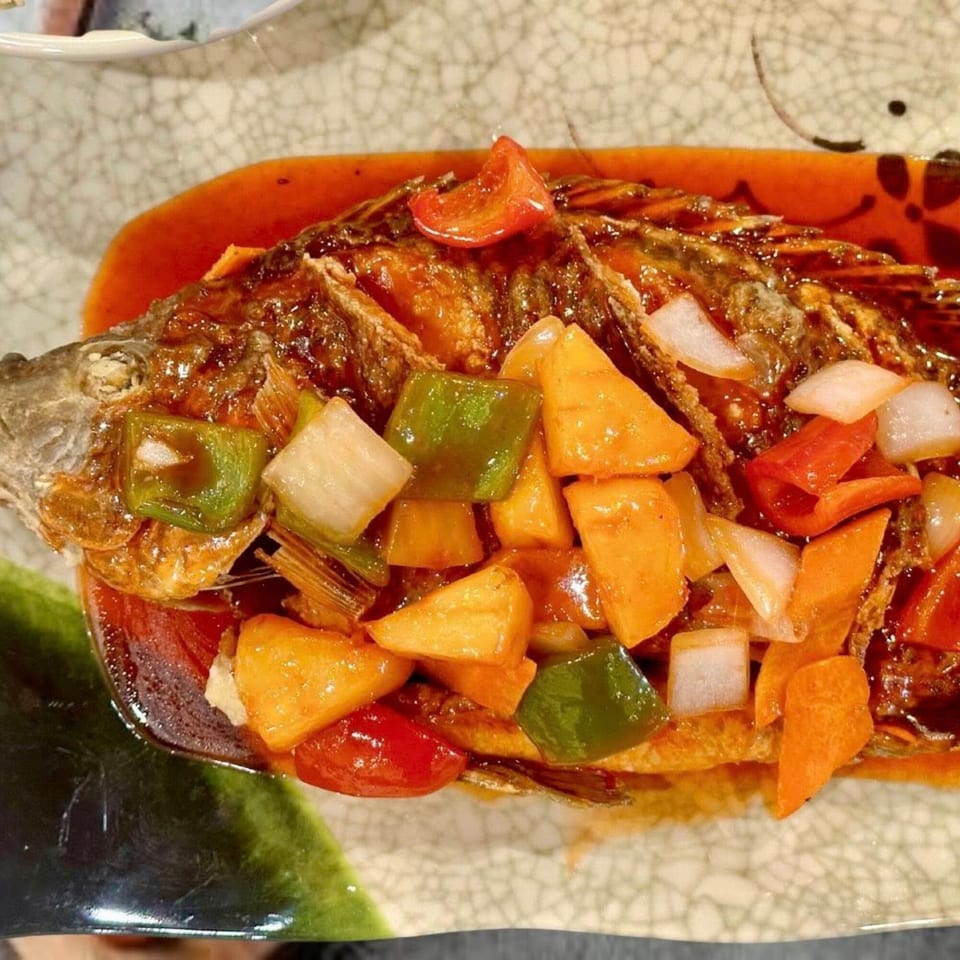 Whole fried fish with sweet and sour sauce, bell peppers, and onions on a patterned plate.