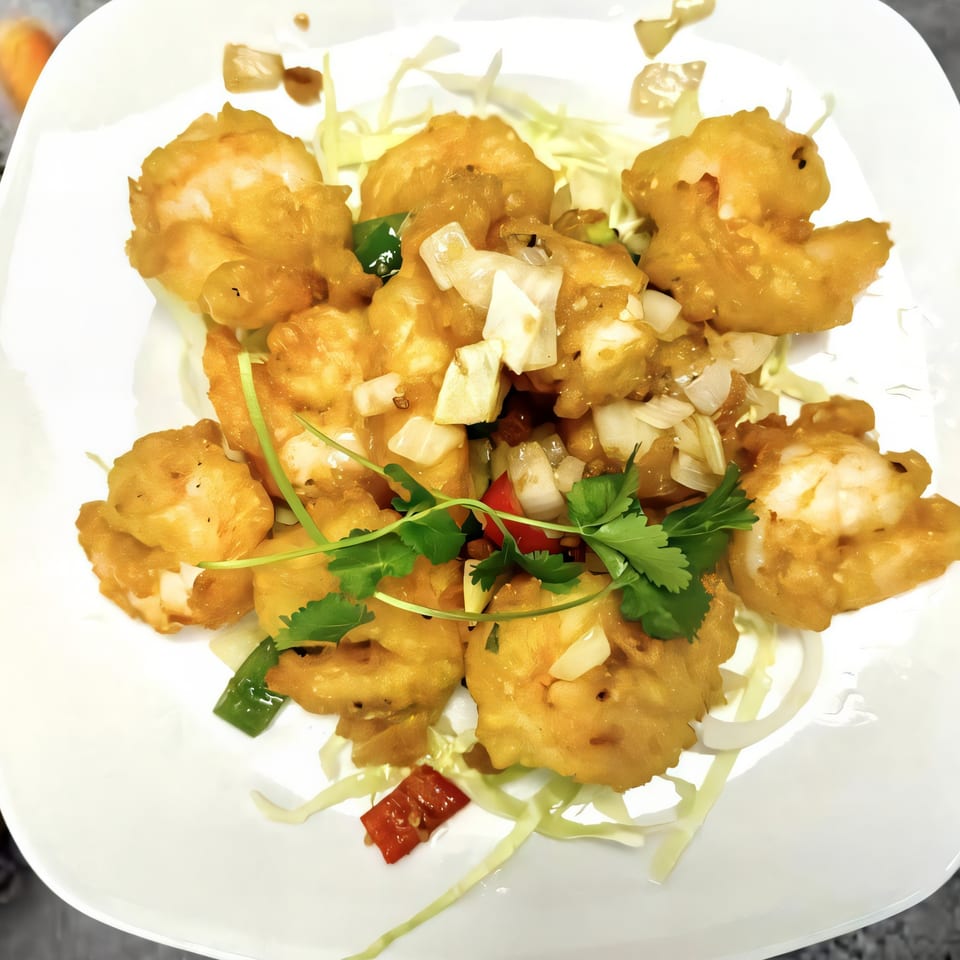 Golden fried shrimp with diced onions, red peppers, and cilantro on a bed of shredded cabbage.