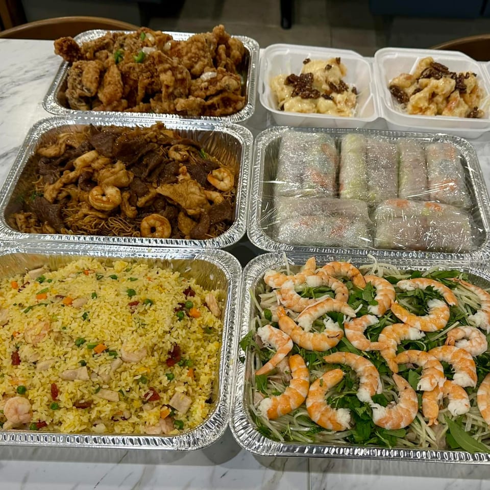 A catering spread from Kin's Restaurant with fried chicken, noodles, fried rice, spring rolls, and shrimp salad.