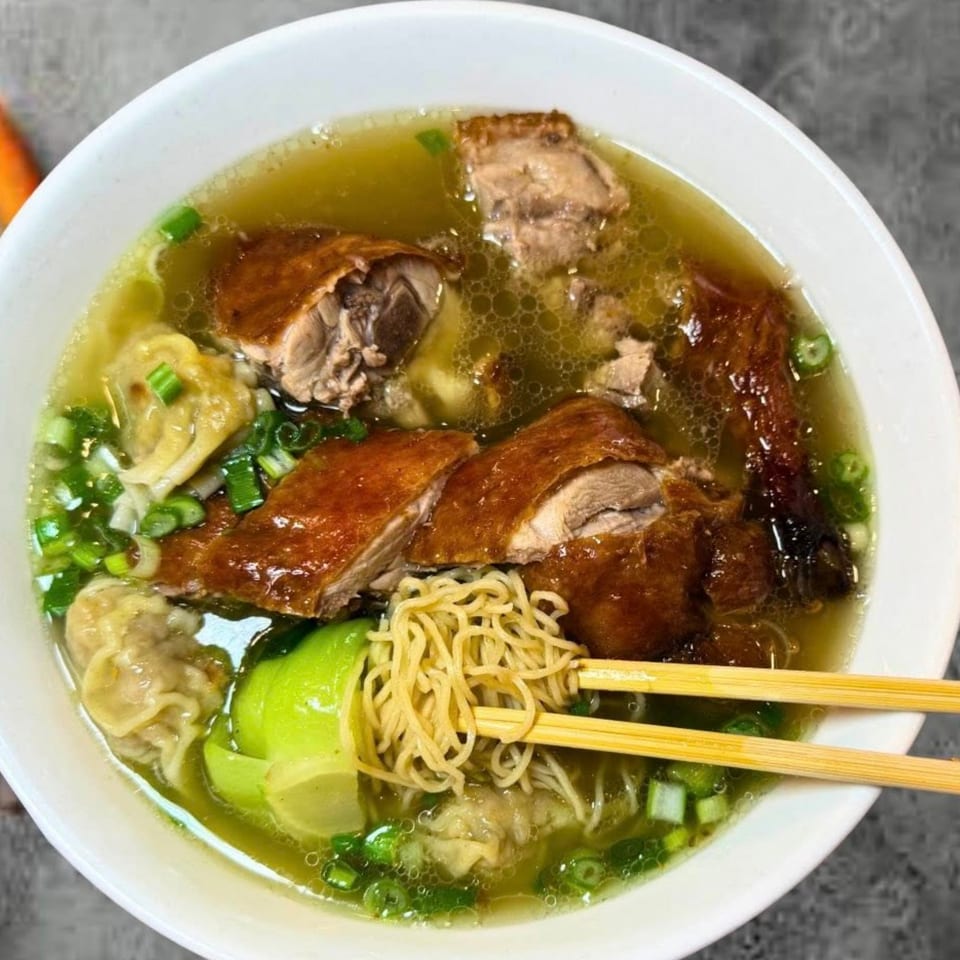 A bowl of Kin's Restaurant's duck noodle soup with wontons, bok choy, and scallions, with chopsticks.